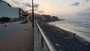 A coastal walkway with a pebbled beach, a promenade with buildings, and a view of the ocean. - Historical house facing the sea in Finca de Plataneras. (San Andrés)