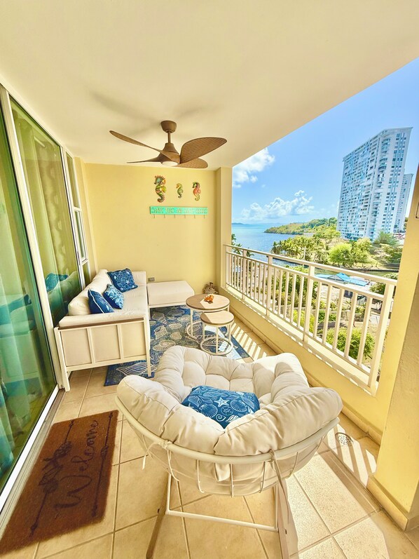 A balcony with a white cushioned seating area, a small round table, and a decorative wall sign.