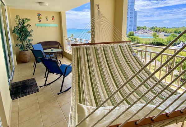 A balcony with a hammock, chairs, a table, and a potted plant. - Lovely apartment with stunning ocean and marina views (Fajardo)