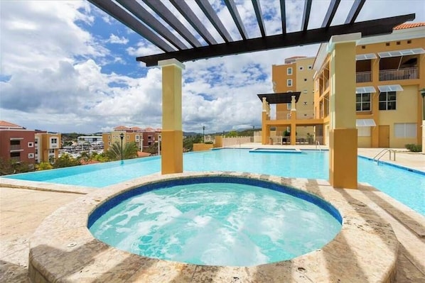 Une piscine sur le toit, avec un jacuzzi, entourée d’immeubles jaunes dotés de balcons.