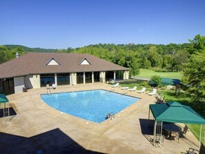 A swimming pool with lounge chairs and umbrellas, a covered patio, and a view of a golf course. - Close to Outdoor Pool, Jetted Tub, Rustic Lodge! (Reeds Spring)