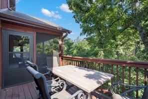 A wooden deck with a table and chairs, overlooking a lush green forest. - Close to Outdoor Pool, Jetted Tub, Rustic Lodge! (Reeds Spring)