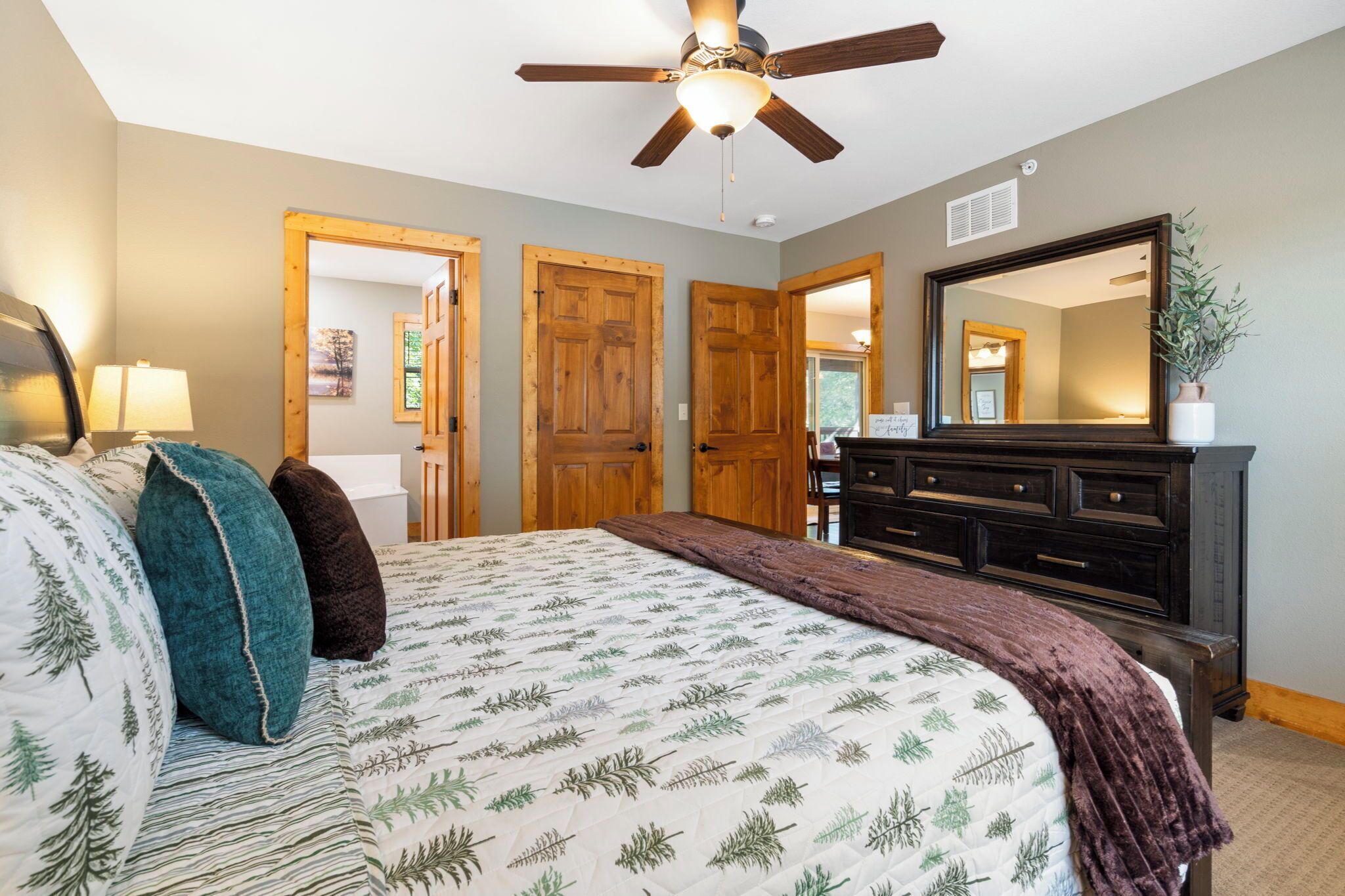 A bedroom with a bed, wooden doors, a dresser, and a ceiling fan.