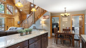 A kitchen with wooden cabinets, granite countertops, and a dining area with wooden chairs and a table. - Close to Outdoor Pool, Jetted Tub, Rustic Lodge! (Reeds Spring)