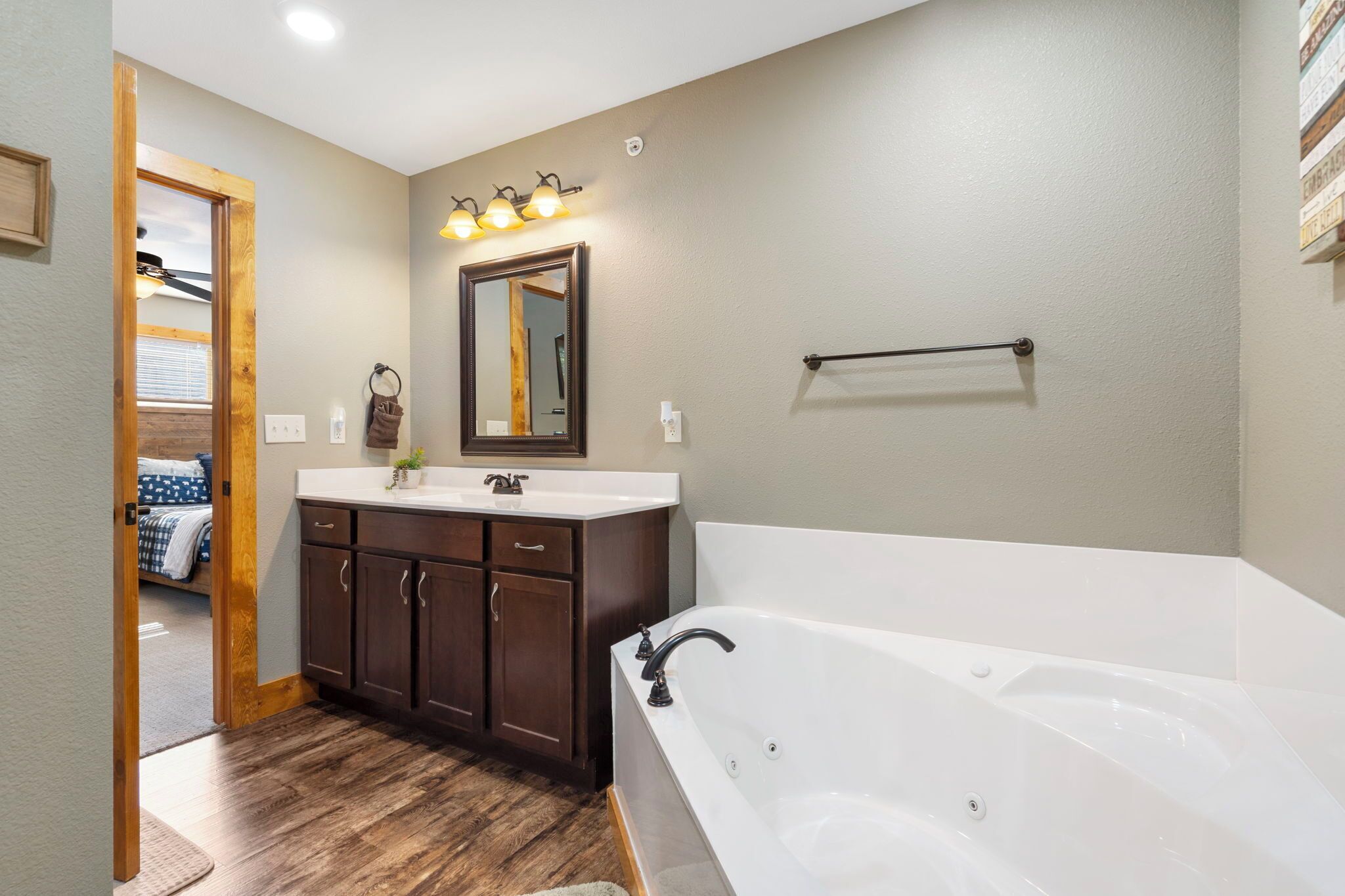 A modern bathroom with a large bathtub, dark wooden cabinets, a white sink, and a mirror with lights above it.