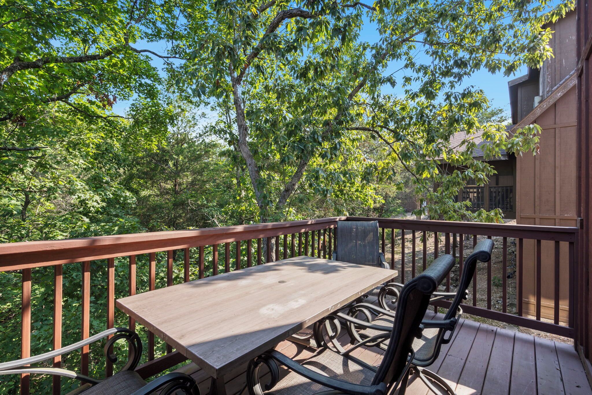 A wooden deck with a table and chairs, surrounded by trees and a building.