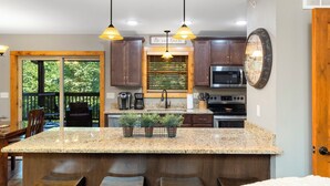A kitchen with granite countertops, wooden cabinets, and pendant lighting. There is a large window with a view of greenery outside. - Close to Outdoor Pool, Jetted Tub, Rustic Lodge! (Reeds Spring)