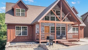 A two-story house with a stone facade, a wooden porch, and a garage. - Close to Outdoor Pool, Jetted Tub, Rustic Lodge! (Reeds Spring)