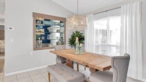 A dining area with a wooden table, cushioned chairs, a chandelier, and a decorative mirror. - Beachcomber Bungalow: Slow Down, East of A1A, Heated Pool, Hot Tub & Beach Gear (Vero Beach)