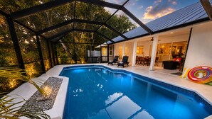 A swimming pool with a glass enclosure, surrounded by a patio area with outdoor furniture and a view of the house. - Beachcomber Bungalow: Slow Down, East of A1A, Heated Pool, Hot Tub & Beach Gear (Vero Beach)