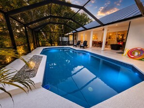 A swimming pool with a glass enclosure, surrounded by a patio area with outdoor furniture and a view of the house.