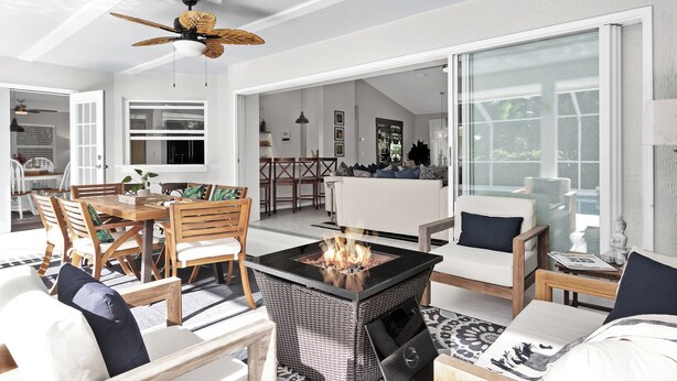 A modern living room with a fireplace, wicker furniture, and a large glass door leading to an outdoor area. - Beachcomber Bungalow: Slow Down, East of A1A, Heated Pool, Hot Tub & Beach Gear (Vero Beach)