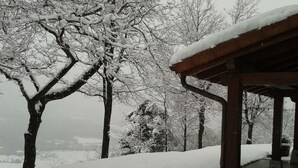 Un espace extérieur enneigé, doté d’une structure en bois, peut-être un belvédère, et d’arbres chargés de neige.
