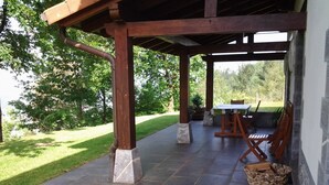 Un patio couvert avec une table et des chaises, un sol en pierre et une pelouse.