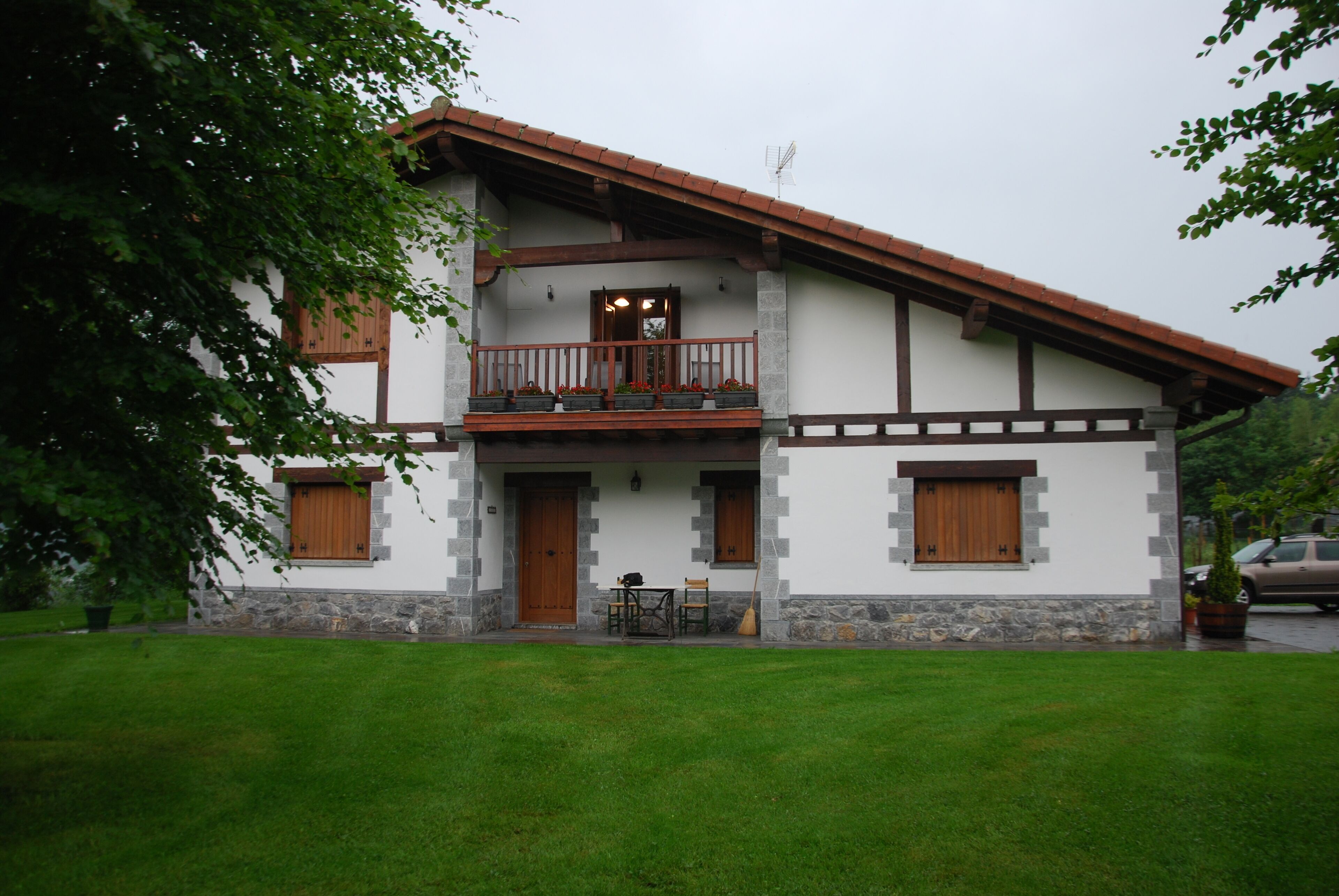 A two-story house with a balcony, stone foundation, and wooden doors.