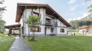 Une maison à deux étages avec une façade en pierre, un balcon en bois et un chemin en pierre menant à l’entrée.