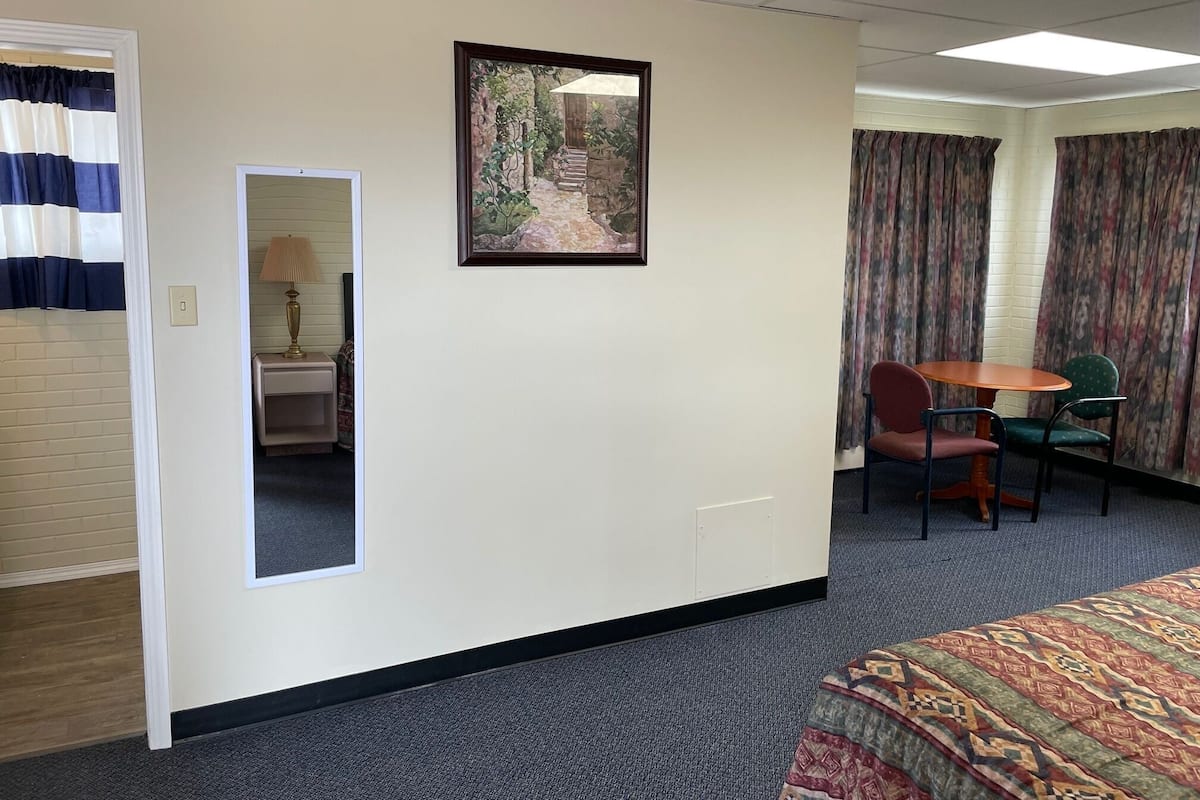A hotel room with a bed, a small table with chairs, a painting on the wall, and a door leading to another room.