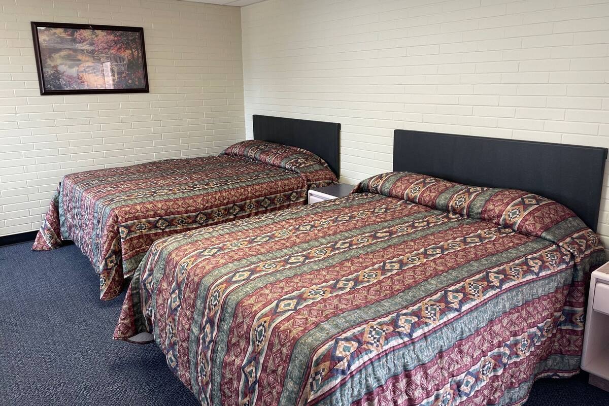 A hotel room with two beds, a white brick wall, and a framed picture on the wall.