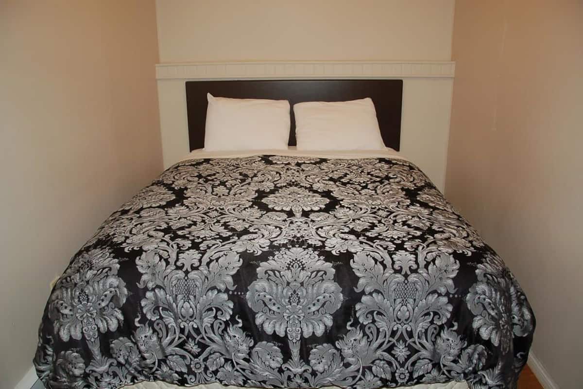 A bed with a black and white damask bedspread and two white pillows.