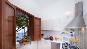 A kitchen with white cabinets, a stove, a sink, and a window with a view of the sea.