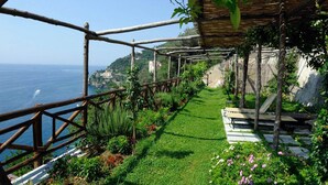 A garden pathway with a view of the sea, wooden pergolas, and a bench.