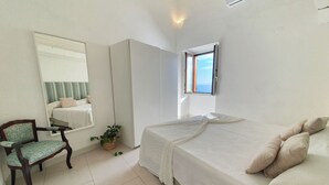 A bedroom with a bed, a chair, a potted plant, a mirror, and a window.