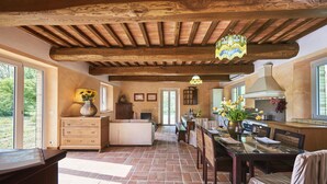 A spacious kitchen with a dining area, wooden ceiling beams, and large windows.