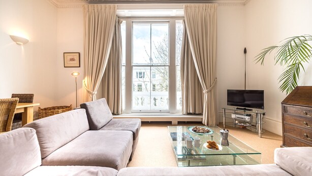 A modern living room with a sofa, a glass coffee table, a TV, and a plant.