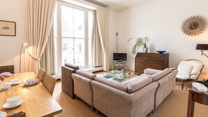 A living room with a sofa, a coffee table, a TV, a dining table with chairs, and a plant.