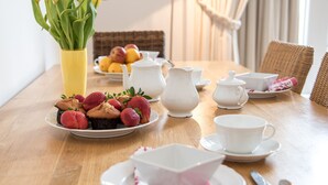 A dining table with white ceramic tea sets, plates of strawberries and muffins, and a vase of yellow tulips.