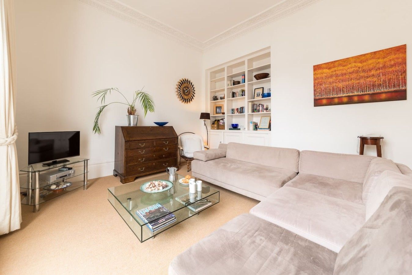 Un salon comprenant un canapé, une table basse en verre, un téléviseur, une bibliothèque et un tableau accroché au mur.