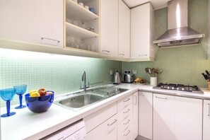 Une cuisine avec des meubles blancs, un évier en acier inoxydable, une cuisinière à gaz et un dosseret de carrelage vert.