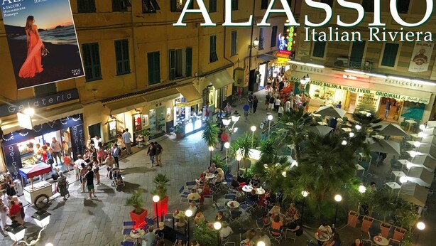 Un espace café animé en plein air, avec des tables et des chaises, entouré d’immeubles et de boutiques.