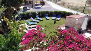 Une cour avec des chaises longues, un mur en pierre et des fleurs de bougainvillier.