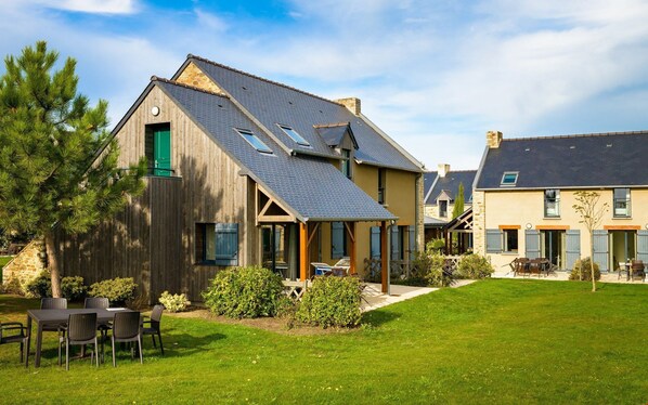 A residential building with a sloped roof, wooden exterior, and a small front porch with outdoor seating.