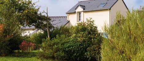 A single-story house with a sloped roof, surrounded by lush greenery and a well-maintained lawn.