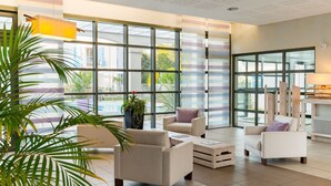 Eine großzügige Lobby mit großen Fenstern, Blick auf den Pool und modernen Möbeln.