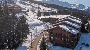 Een bergresort bedekt met sneeuw, met meerdere gebouwen, waaronder een opvallend hotel met balkons en een skilift op de achtergrond.
