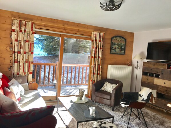 Ein gemütliches Wohnzimmer mit Sofa, Sessel und Couchtisch, einem Fernseher und einem Kamin.