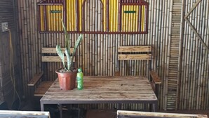 A bamboo wall with a colorful, stylized building structure. There is a table with chairs in front of the wall. - Tamcoc White Swan Hostel (Nam Hoa Lu)