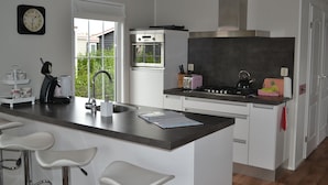 Une cuisine moderne dotée d’un îlot central, de meubles blancs, d’appareils électroménagers en acier inoxydable et offrant une vue sur l’extérieur.