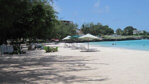Ein Strand mit Liegestühlen und Sonnenschirmen, ein klarer, blauer Himmel und ein Gebäude im Hintergrund.