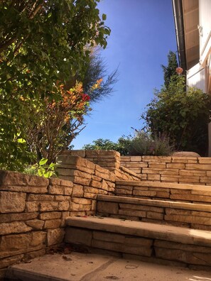 Una scala in pietra conduce a un edificio, circondato da vegetazione e un cielo azzurro intenso.
