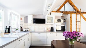 A modern kitchen with white cabinets, a wooden ceiling, and a dining table with a vase of flowers.