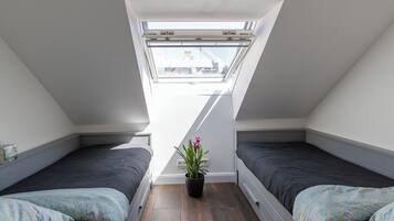 Ein kleines, helles Schlafzimmer im Dachgeschoss mit zwei Betten, einem Dachfenster und einer Topfpflanze.