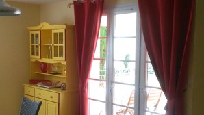 A room with a dining table, chairs, a yellow cabinet, and a sliding glass door with red curtains.