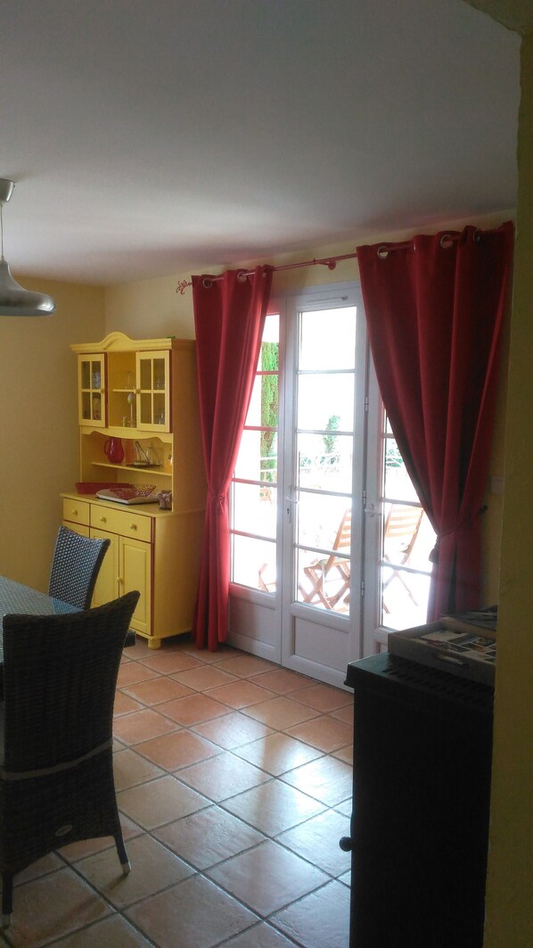 A room with a dining table, chairs, a yellow cabinet, and a sliding glass door with red curtains. - OLIVE TREES IN COTIGNAC (VAR) (Cotignac)