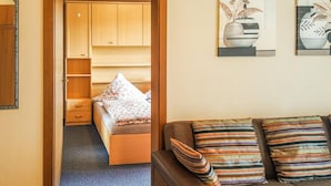 Une pièce de taille modeste, comprenant un lit, un canapé et une armoire en bois. Deux œuvres d’art sont accrochées au mur.