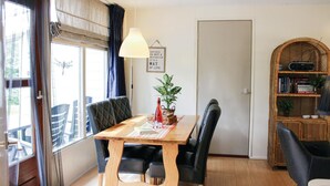 A dining area with a wooden table, black upholstered chairs, a potted plant, and a bookshelf.