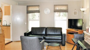 A living room with a black leather sofa, a wooden coffee table, a TV, and a kitchen area visible through an open door.
